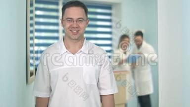 <strong>微笑男医生</strong>戴着眼镜看着摄像机，而医务人员则在后台工作